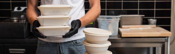 cropped view of man in t-shirt with volunteer lettering holding plastic containers in kitchen, banner - Фото, изображение