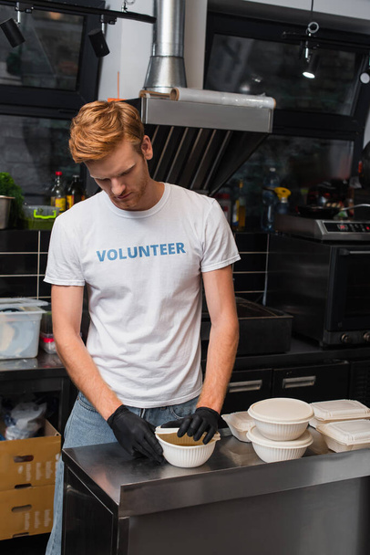 redhead volunteer covering bowl with plastic cup in kitchen  - Photo, image