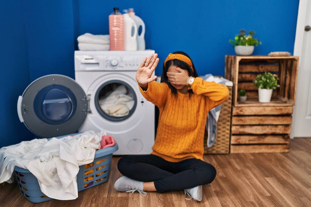 Jeune femme hispanique faire la lessive couvrant les yeux avec les mains et faire arrêter geste avec expression triste et peur. concept embarrassé et négatif.  - Photo, image