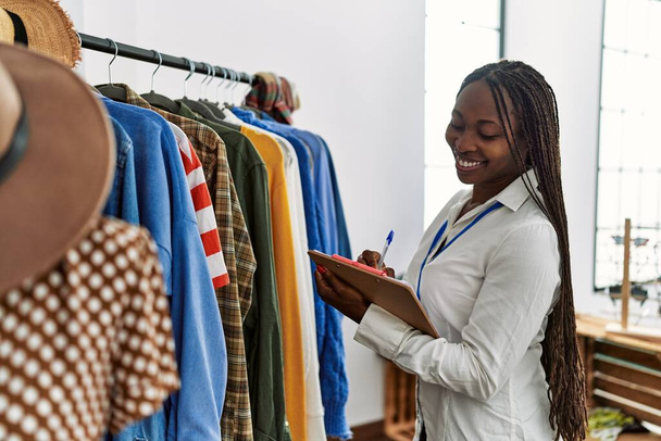 Młoda afrykańska sklepikarka uśmiecha się szczęśliwa pracując w sklepie odzieżowym. - Zdjęcie, obraz