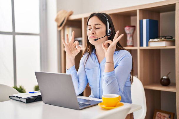Young brunette woman wearing call center agent headset relax and smiling with eyes closed doing meditation gesture with fingers. yoga concept.  - Photo, image