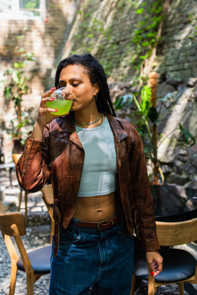 young african american woman in leather jacket drinking green cocktail outside - Foto, immagini