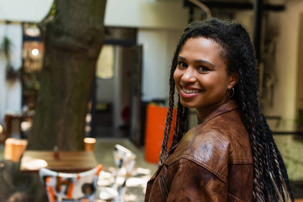 joyful african american woman in brown leather jacket smiling outside - Fotó, kép