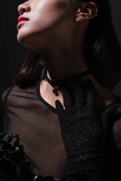cropped view of brunette young woman in black glove touching neck isolated on black - Photo, image