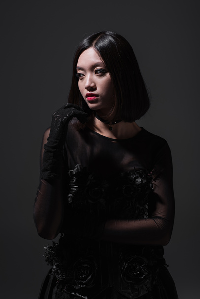 brunette asian model in black gothic outfit and gloves isolated on dark grey - Foto, Imagen