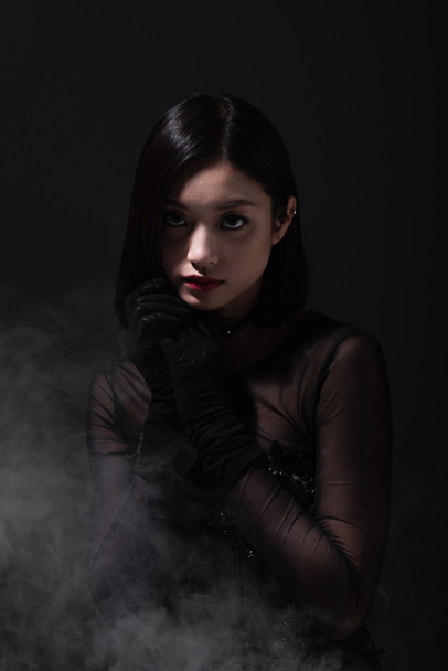 portrait of young asian woman in gothic outfit and gloves on grey with smoke - Foto, Imagem