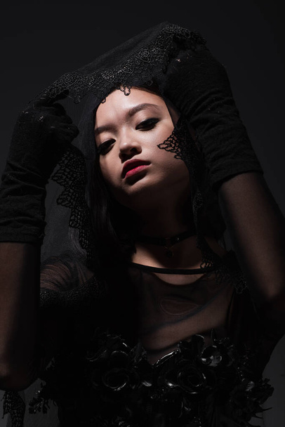 portrait of asian model in black gloves holding black veil isolated on grey - Foto, imagen