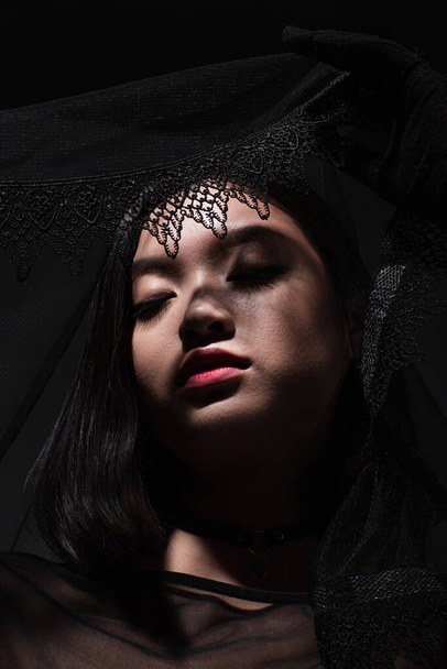 портрет молодой азиатки в черных перчатках, держащей черную вуаль, изолированную на сером - Фото, изображение