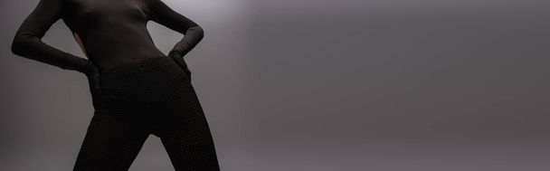 обрізаний вид моделі в чорному вбранні з рукавичками позує руками на стегнах ізольовано на сірому, банер
 - Фото, зображення