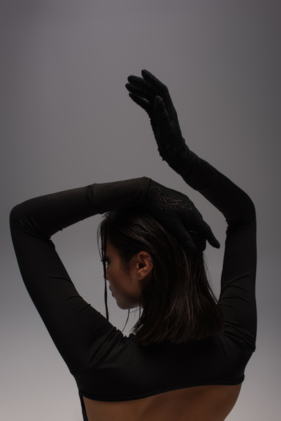 вид ззаду чуттєвої азіатки в загальному чорному вбранні з рукавичками жестикуляція ізольована на сірому
  - Фото, зображення