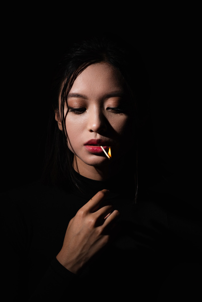 portrait of pretty asian model with burning matchstick in mouth isolated on black - Foto, afbeelding