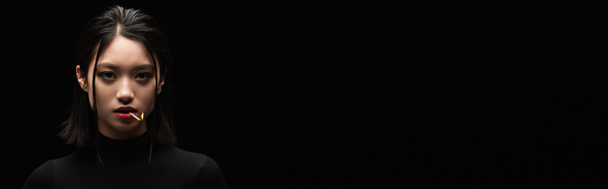 портрет красивої азіатки з палаючою сірниковою стрічкою в роті, дивлячись на камеру ізольовано на чорному, банер
 - Фото, зображення