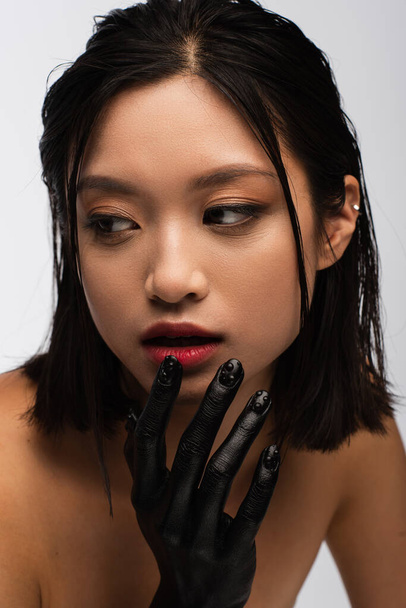 portrait of young asian woman with bare shoulders and hand in black paint posing isolated on grey - Foto, afbeelding