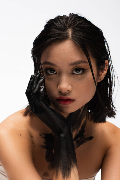 brunette young asian woman with hand in black paint looking at camera isolated on white - Fotografie, Obrázek