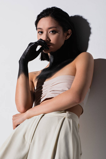 young asian woman with hand in black paint looking at camera on white - Foto, Imagem