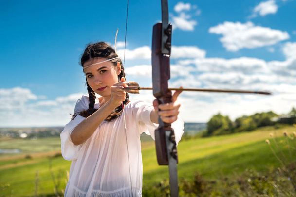 pretty hunter girl shooting bow and arrow  in the grassland  - Photo, Image