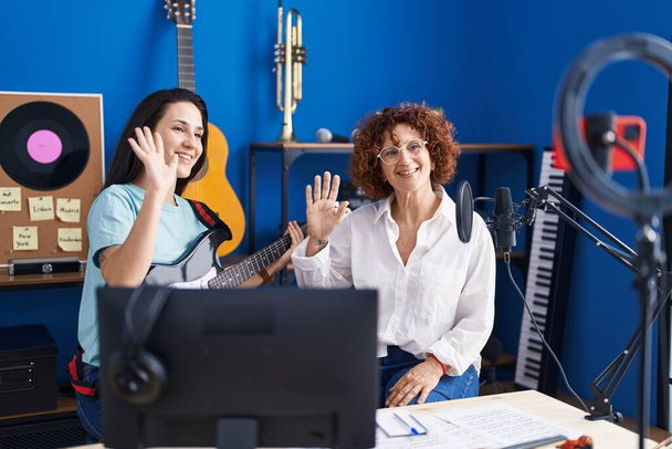 Две женщины-музыкантки на онлайн-уроке электрогитары на смартфоне в музыкальной студии - Фото, изображение