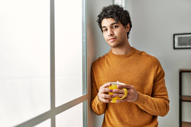 Young hispanic man drinking coffee standing at home. - Фото, изображение