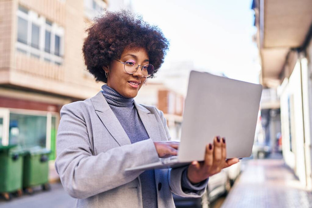Afrikaans amerikaanse vrouw executive glimlachen zelfverzekerd met behulp van laptop op straat - Foto, afbeelding
