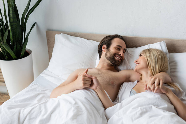щасливі коханці тримаються за руки і посміхаються один одному на ліжку вранці
 - Фото, зображення