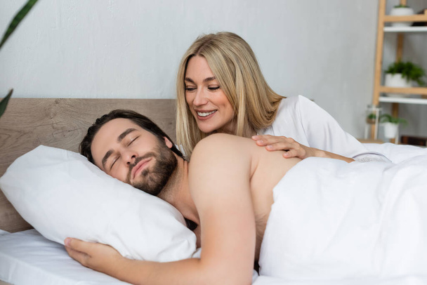 happy blonde woman waking sleeping lover in morning - Photo, Image