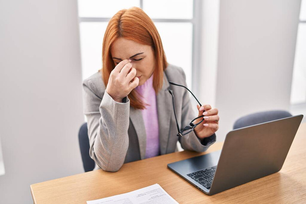 Jonge blanke vrouw zakenman gestrest met behulp van laptop op kantoor - Foto, afbeelding