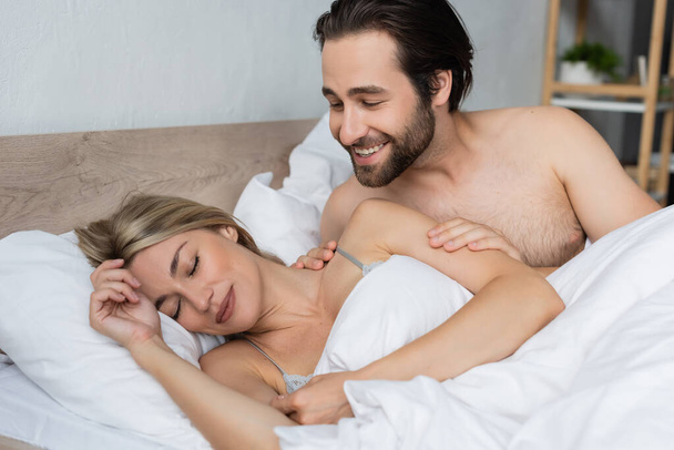 smiling unshaven man waking blonde woman sleeping in morning - Foto, Bild