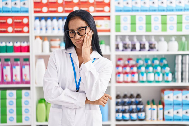 Mujer hispana que trabaja en farmacia pensando que se ve cansada y aburrida con problemas de depresión con los brazos cruzados.  - Foto, Imagen