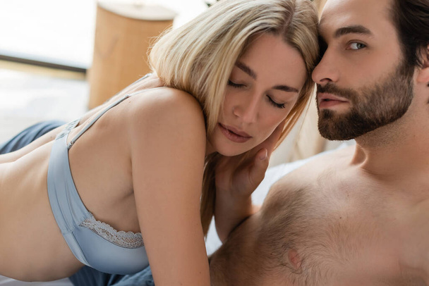 shirtless man looking at camera near hot blonde woman with closed eyes - Zdjęcie, obraz