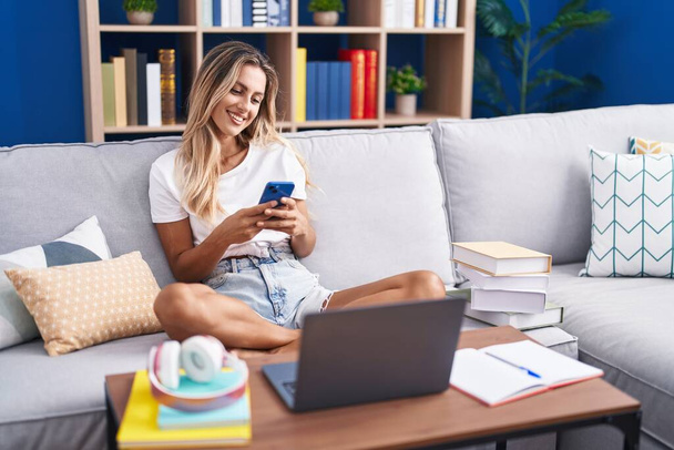 Mladá blondýna žena student sedí na pohovce pomocí smartphone doma - Fotografie, Obrázek