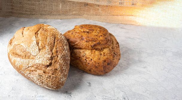 Ιστορικό δύο λοστών ψωμιού ολικής άλεσης σε μια ρουστίκ επιφάνεια. ψωμί δημητριακών - Φωτογραφία, εικόνα