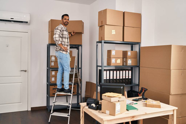 Jeune homme hispanique ecommerce travailleur d'affaires debout sur l'échelle au bureau - Photo, image