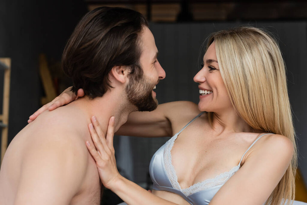 sexy woman in bra and shirtless bearded man smiling at each other in bedroom - Foto, Bild