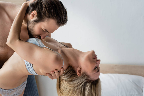 side view of brunette man kissing breast of passionate blonde woman in underwear - Foto, Bild