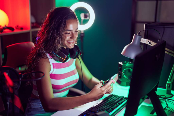 Fiatal gyönyörű spanyol nő streamer segítségével számítógép és okostelefon a játékteremben - Fotó, kép
