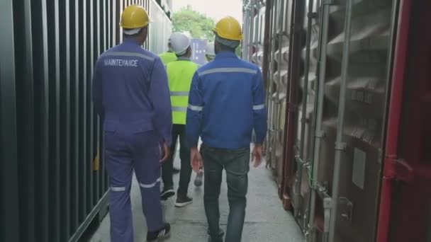 Group of multiracial workers in safety uniforms and hardhats walk and inspect shipping cargo with White male manager at nook of container stack, import and export goods logistic transport industry.  - Materiał filmowy, wideo