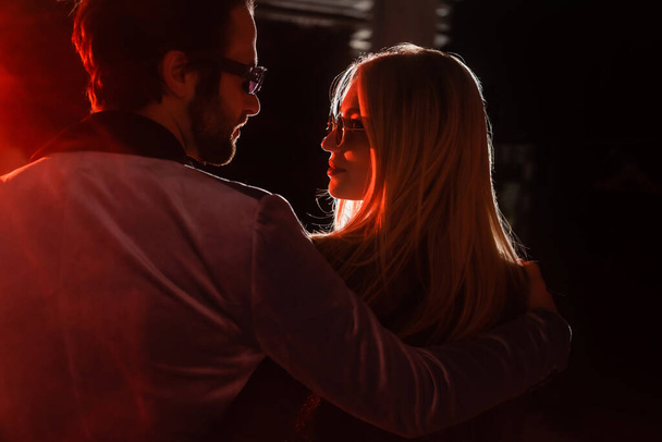couple in trendy eyeglasses looking at each other at night party in darkness with light - Foto, Imagen