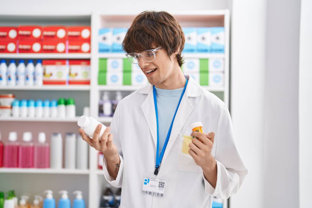 Young blond man pharmacist smiling confident holding pills bottles at pharmacy - Φωτογραφία, εικόνα