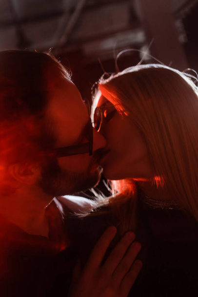 Низкий угол обзора пары в солнцезащитных очках поцелуи во время вечеринки с освещением  - Фото, изображение