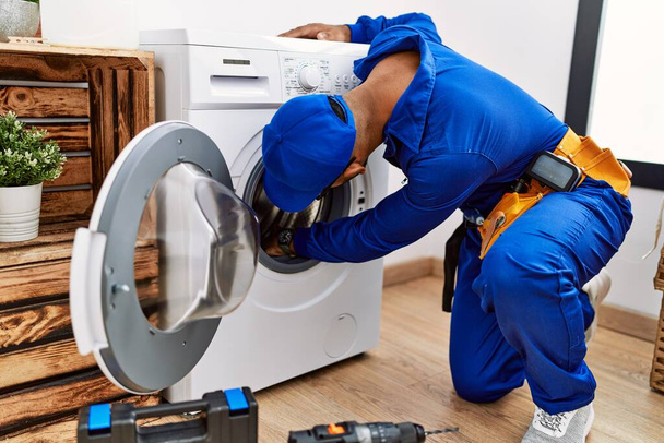 Young arab man wearing technician uniform repairing washing machine at laundry room - Foto, afbeelding