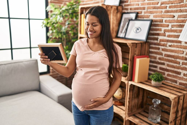 Young latin woman pregnant looking photo at home - Photo, Image