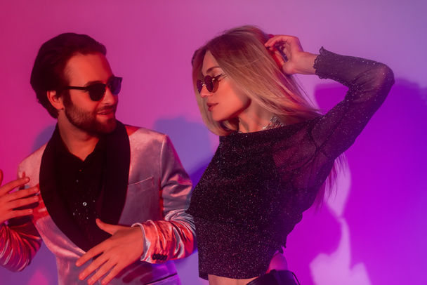 Stylish couple in sunglasses dancing during party on purple background  - Fotó, kép