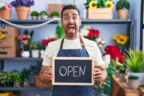 Hispanic man with beard working at florist holding open sign celebrating crazy and amazed for success with open eyes screaming excited.  - Photo, Image