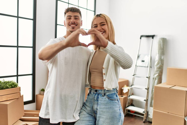 Молода біла пара посміхається щасливо роблячи символ серця руками в новому будинку
. - Фото, зображення