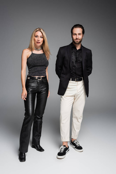 Full length of stylish couple looking at camera on grey background  - Foto, Imagen