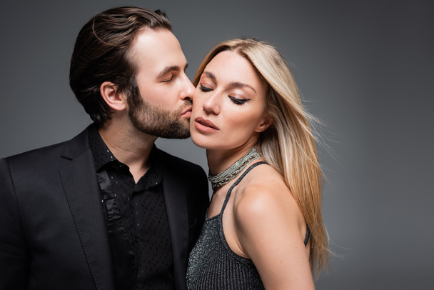 Man in jacket kissing stylish blonde girlfriend isolated on grey  - Фото, зображення