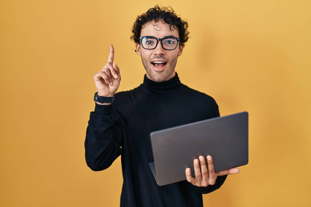 Hispanic man working using computer laptop surprised with an idea or question pointing finger with happy face, number one  - Fotoğraf, Görsel