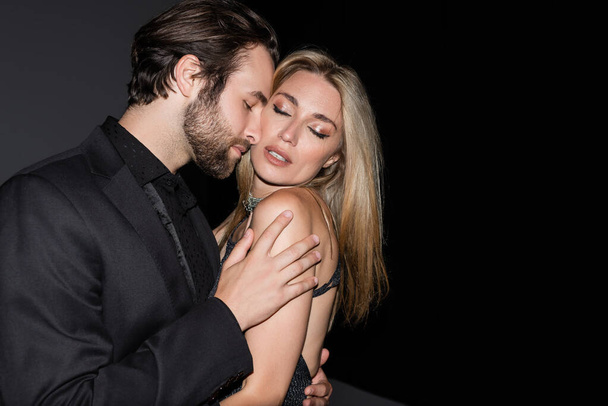 Bearded man touching sensual blonde girlfriend on dark background  - Foto, afbeelding