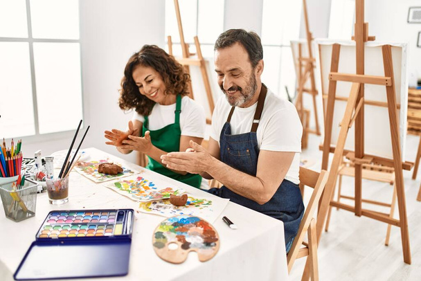 Двоє студентів середнього віку посміхаються щасливі моделювання глини, сидячи на столі в художній школі
. - Фото, зображення