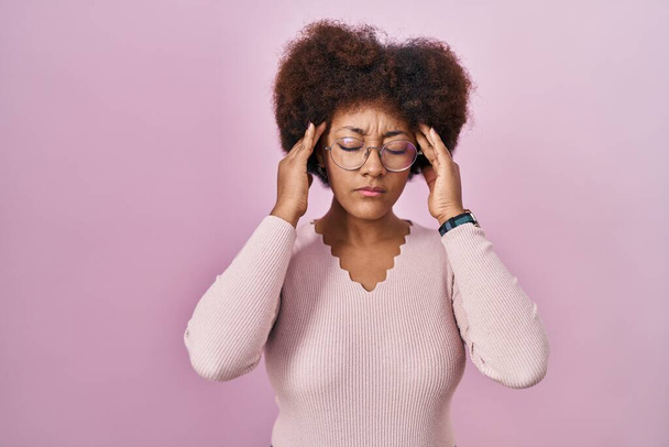 Giovane donna afroamericana in piedi su sfondo rosa con mano sulla testa, mal di testa perché lo stress. emicrania.  - Foto, immagini